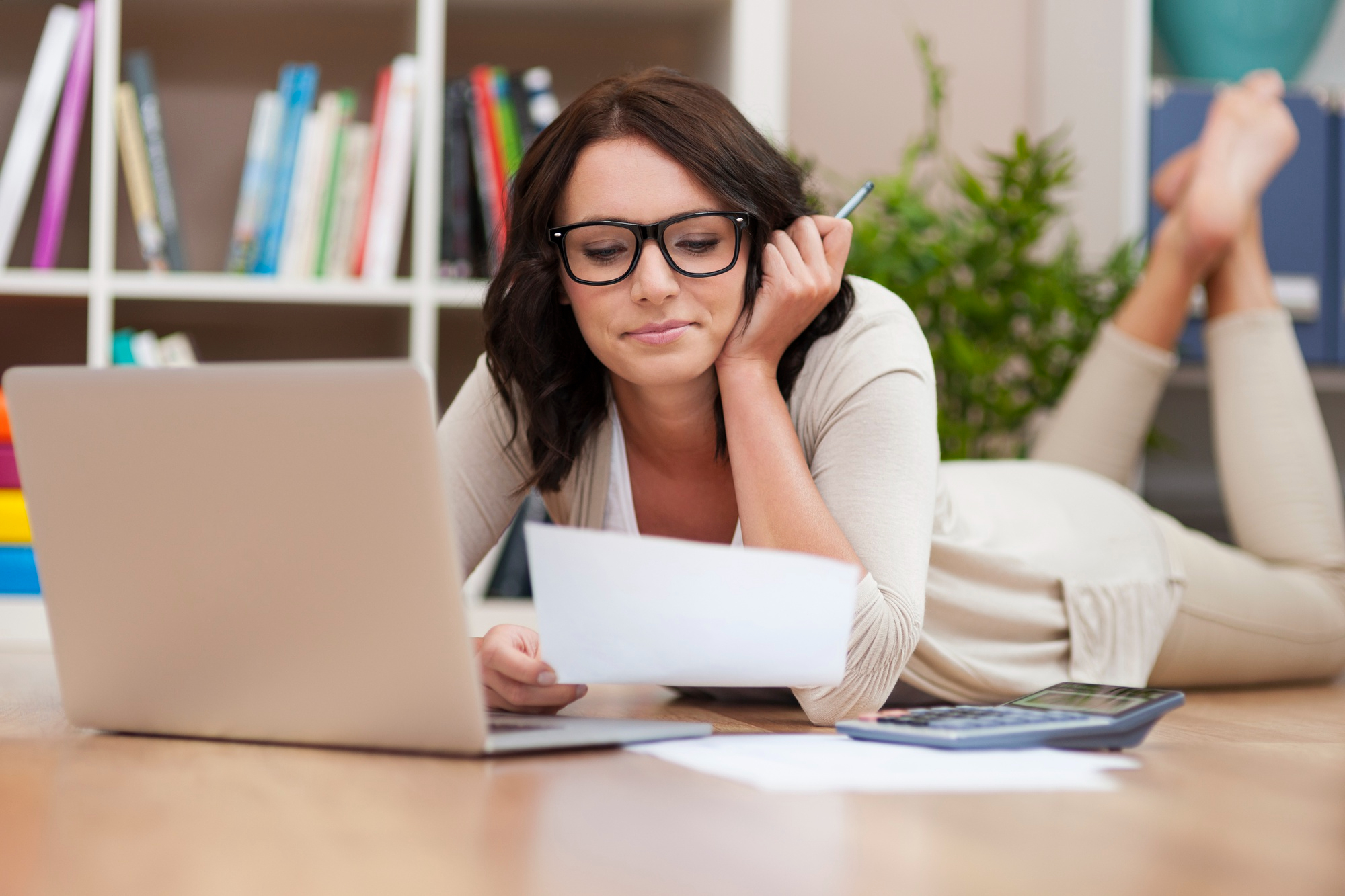 A woman thinking over a laptop, calculator and few sheets of paper